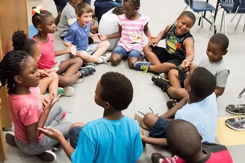 kids in a classroom holding hands, sitting in a circle