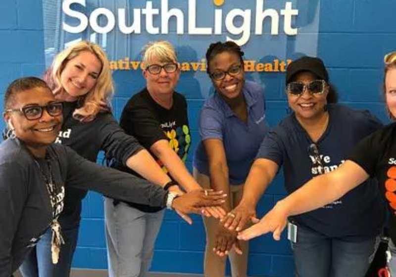 A group of diverse people holding hands in front of a SouthLight Healthcare banner